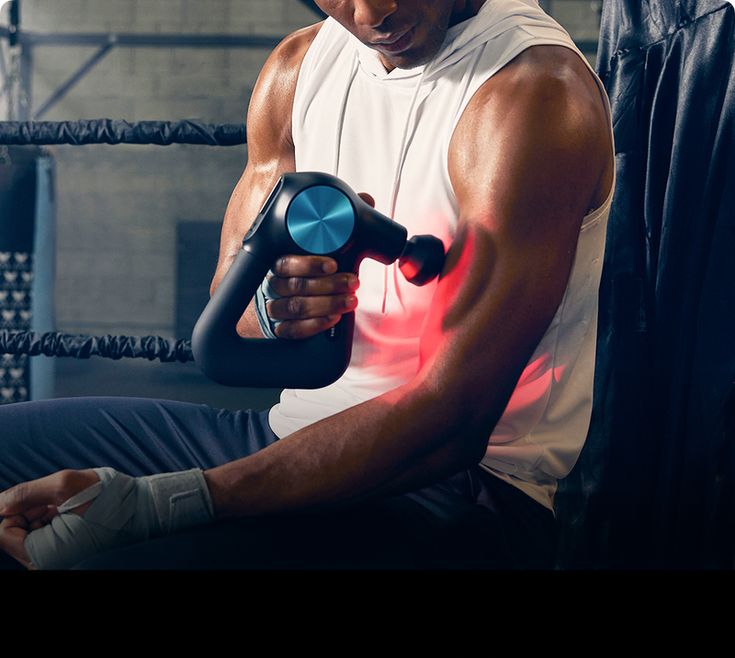 Person using a massage gun on their arm in a gym setting